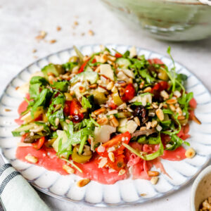 Vooraanzicht van een bord met carpaccio en daarop een grote salade afgewerkt met balsamicocrème