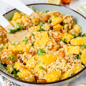 Vooraanzicht van een grote kom couscoussalade met mango, scampi, noten en verse groene kruiden