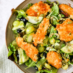 diep bord met een salade met druiven en bosbessen met daarop krokante kip, gepaneerd met panko en goudbruin gebakken.