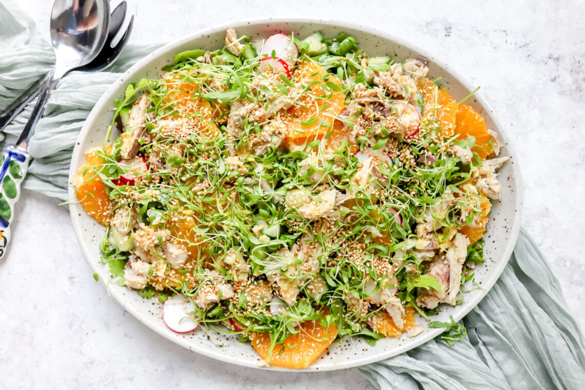 Een grote schotel met een fris ogende salade van rucola, makreel en sinaasappel. Afgewerkt met geroosterde sesamzaadjes, tuinkers en een vinaigrette van mosterd, sinaasappel en olijfolie.
