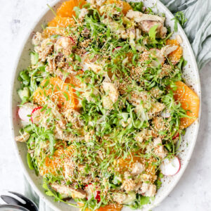grote ovalen schotel met een salade van rucola, makreel en sinaasappel. Afgewerkt met geroosterde sesamzaadjes en tuinkers.