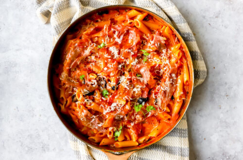 bovenaanzicht van een grote pan met pasta in een romige tomatensaus met wodka. afgewerkt met krokante prosciutto en parmezaan.