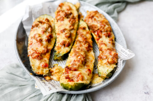 Gehalveerde courgettes op een grote schotel. Gevuld met spaghettisaus met lekker veel kaas erover die goudbruin gebakken werd in de oven.