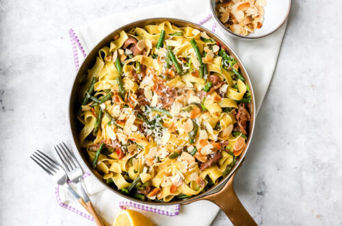 Bovenaanzicht van een grote pan met tagliatelle erin met boontjes, parmaham, rode peper en citroen. Afgewerkt met geroosterde amandelschilfers en parmezaan.
