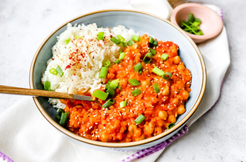 Een groot bord met rijst en rode curry van kikkererwten en rode linzen. Afgewerkt met lente-ui, sesamzaadjes en chilivlokken. Een kleurrijk tafereel!