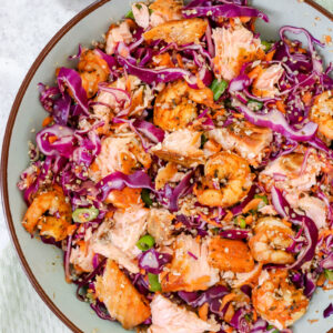 bovenaanzicht van een grote kom met een salade van dun gesneden rode kool, gebakken scampi's en zalm en quinoa en wortel. Afgewerkt met sesamzaadjes