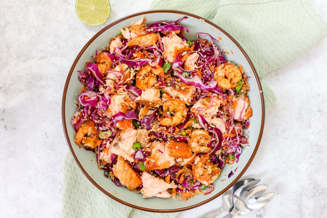bovenaanzicht van een grote kom met een salade van dun gesneden rode kool, gebakken scampi's en zalm en quinoa en wortel. Afgewerkt met sesamzaadjes