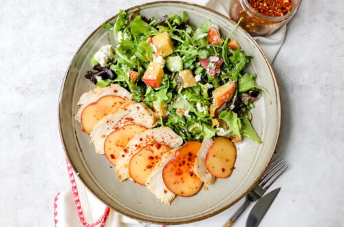 bovenaanzicht van een diep bord met een salade van feta en perzik met daarnaast schijfjes kipfilet en perzik afgewisseld afgewerkt met honing en chilivlokken