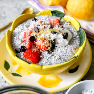 Een gele bloemvorige kom met chiapudding afgewerkt met aardbeien, kokosrasp, chocolate chips en citroenzeste