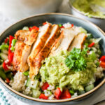 vooraanzicht van een diep bord met parelcouscous met veel groentjes, met schijfjes gebakken kip erop en een lepeltje guacamole