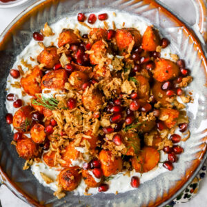 grote schotel met een romige yoghurt-dille dip met daarop krokante harissa patatjes. Afgewerkt met granaatappelpitjes en gefrituurde ui.