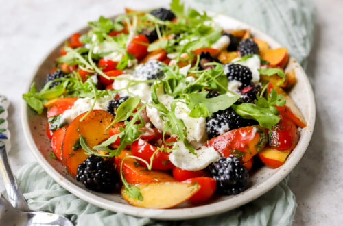 vooraanzicht van een grote schotel met een salade van perzik, kerstomaat en braambessen met balsamicovinaigrette. Afgewerkt met lekker veel burrata en rucol