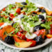vooraanzicht van een grote schotel met een salade van perzik, kerstomaat en braambessen met balsamicovinaigrette. Afgewerkt met lekker veel burrata en rucol