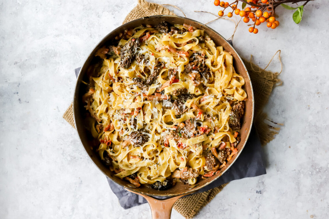 bovenaanzicht van een grote pan met daarin een romige tagliatelle met boschampignons en mascarpone, met spekblokjes, rode peper, bieslook en pecorino.