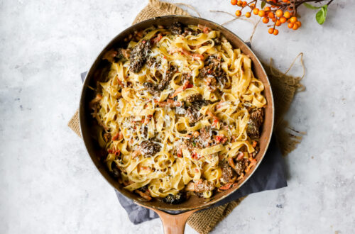 bovenaanzicht van een grote pan met daarin een romige tagliatelle met boschampignons en mascarpone, met spekblokjes, rode peper, bieslook en pecorino.